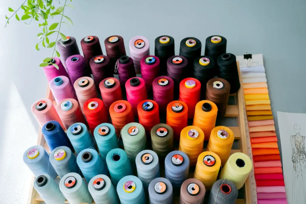 Rayon and metallic thread cones feeding from a vertical thread stand into an embroidery machine