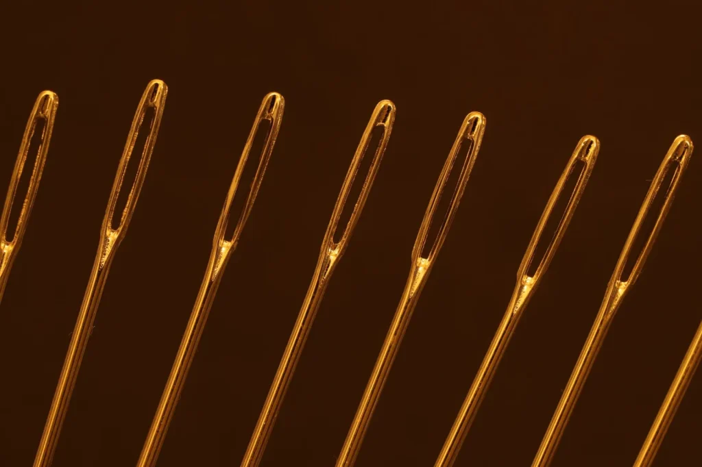 Close up of a topstitch needle threaded with gold metallic thread